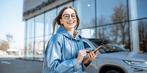 Eine Frau steht vor einem Auto und gibt etwas in ihr Smartphone ein Eine Frau steht vor einem Auto und gibt etwas in ihr Smartphone ein
