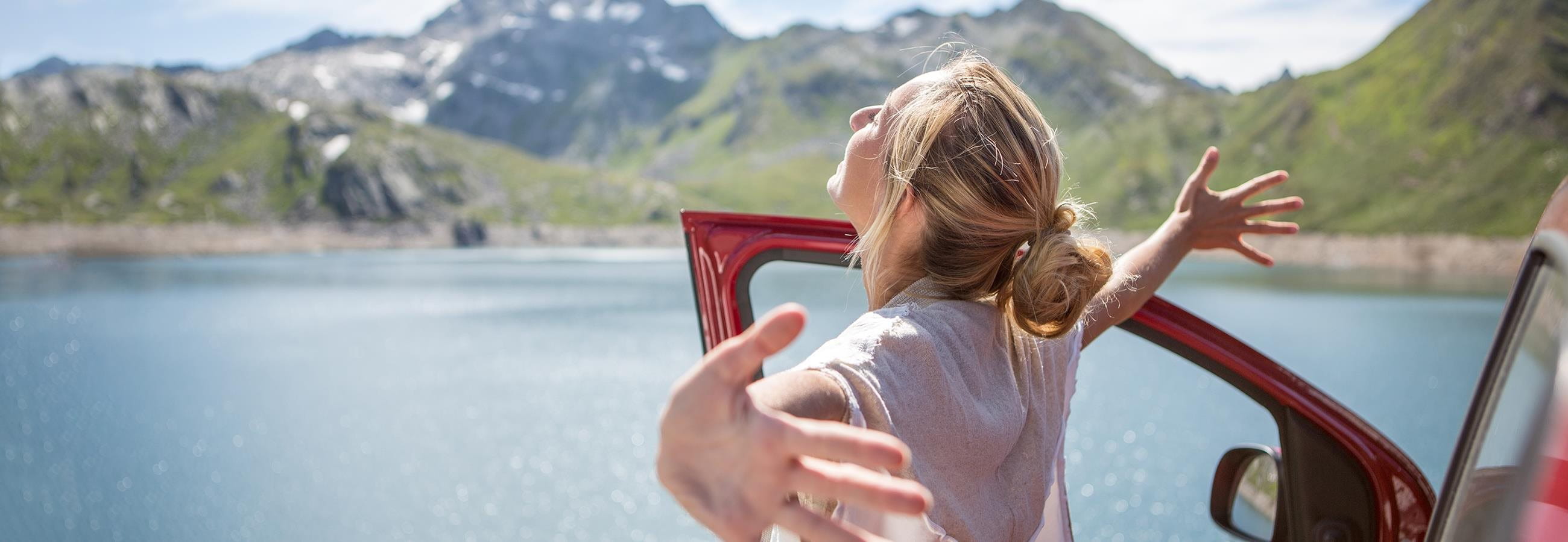 Une femme est debout, les bras écartés, devant sa voiture