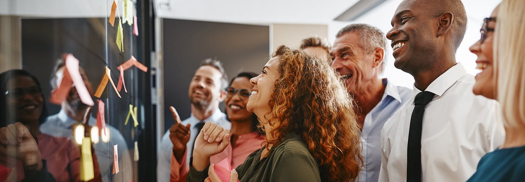 Un gruppo di persone sorride e guarda appunti colorati su un muro.