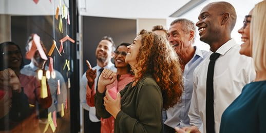 A group of people looks at a wall with colorful sticky notes and smiles. A group of people looks at a wall with colorful sticky notes and smiles.