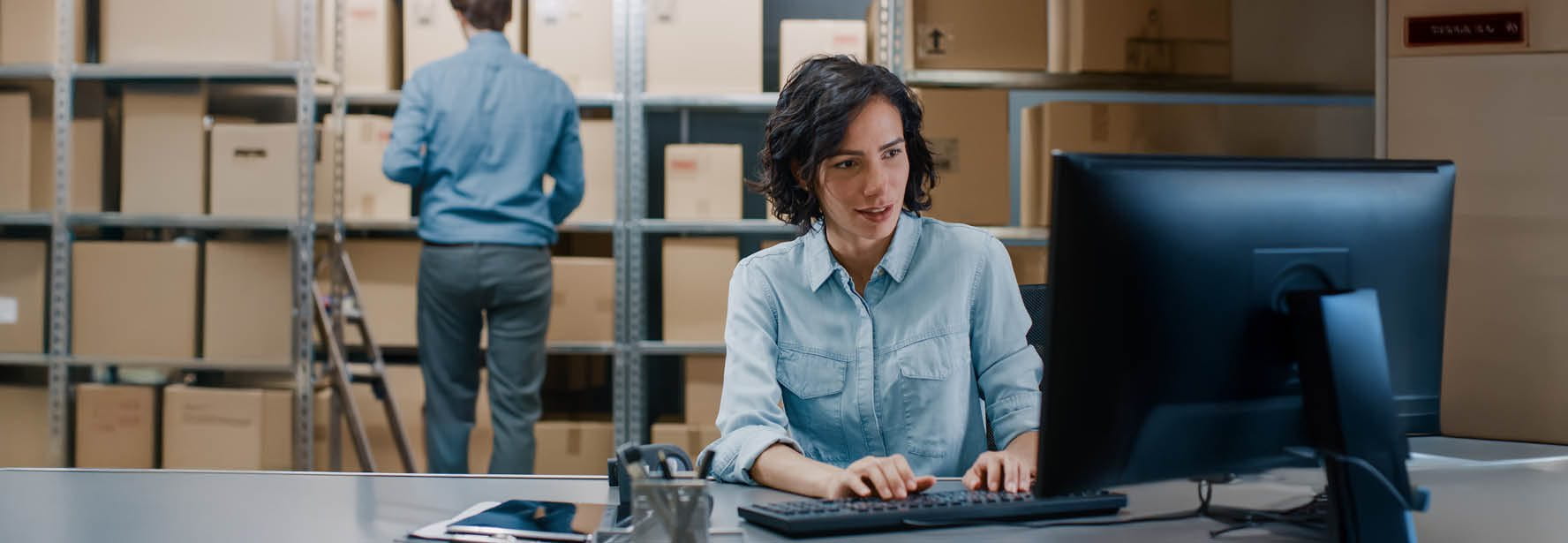 Une femme assise devant son ordinateur dans un entrepôt