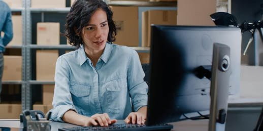 Frau sitzt am Computer in einer Lagerhalle