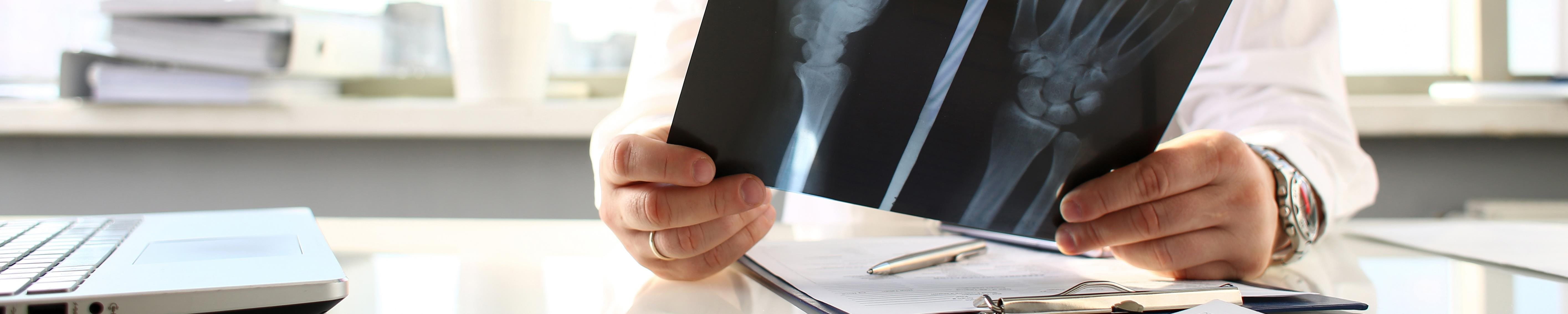 Un médecin s'assied à la table et regarde une image radiographique.