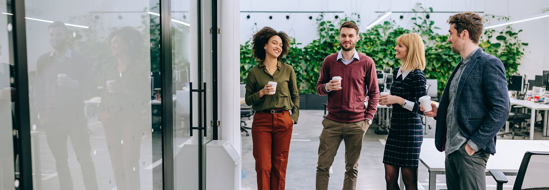 Quattro persone stanno in un moderno ufficio e tengono tazze di caffè.