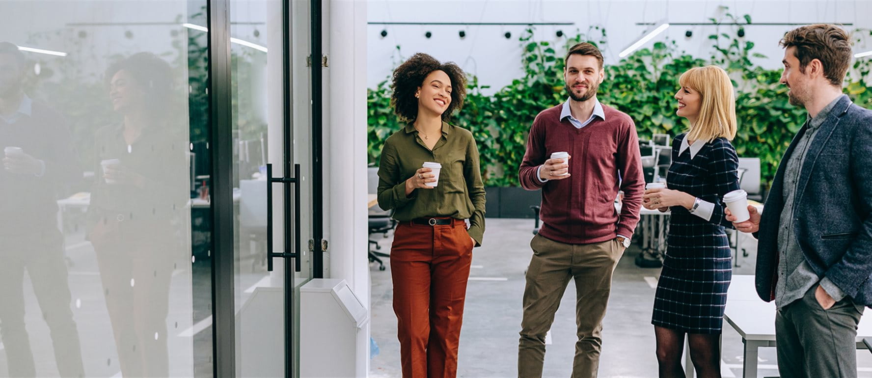 Quattro persone stanno in un moderno ufficio e tengono tazze di caffè. Quattro persone stanno in un moderno ufficio e tengono tazze di caffè.