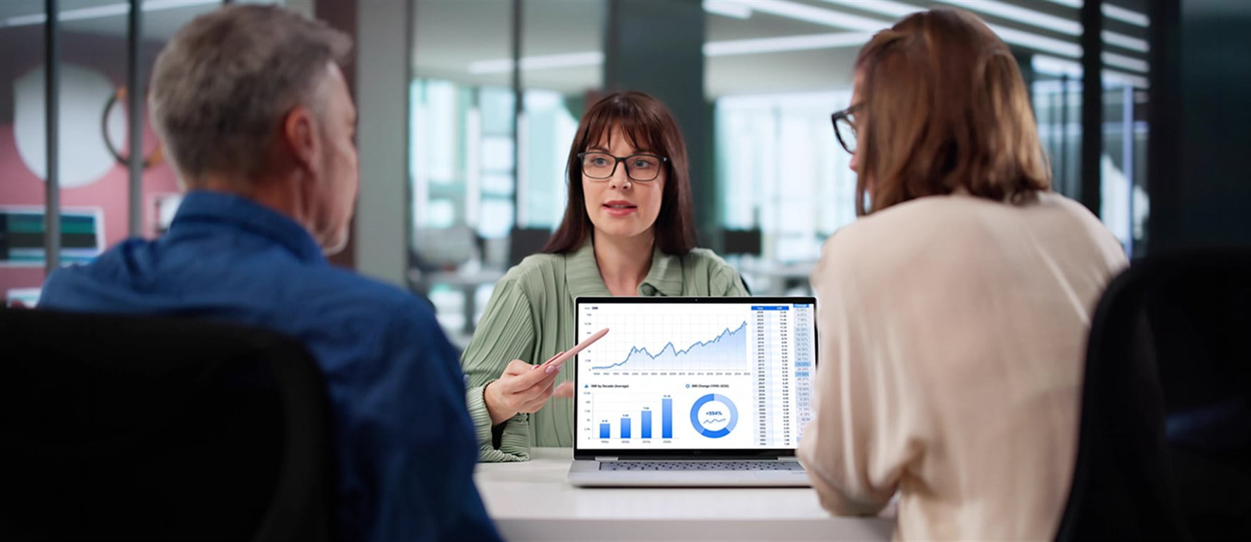Three people in a meeting room, a presentation on a laptop shows charts and data. Three people in a meeting room, a presentation on a laptop shows charts and data.