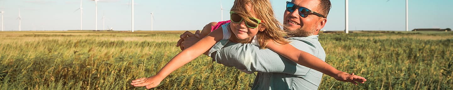 Man with child in a field in front of wind turbines