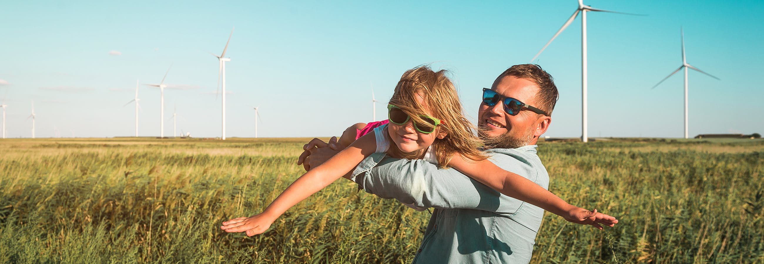 Mann mit Kind auf einem Feld vor Windrädern Mann mit Kind auf einem Feld vor Windrädern