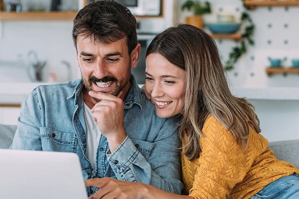 Un couple est assis ensemble sur le canapé et fait la planification financière avec un ordinateur portable