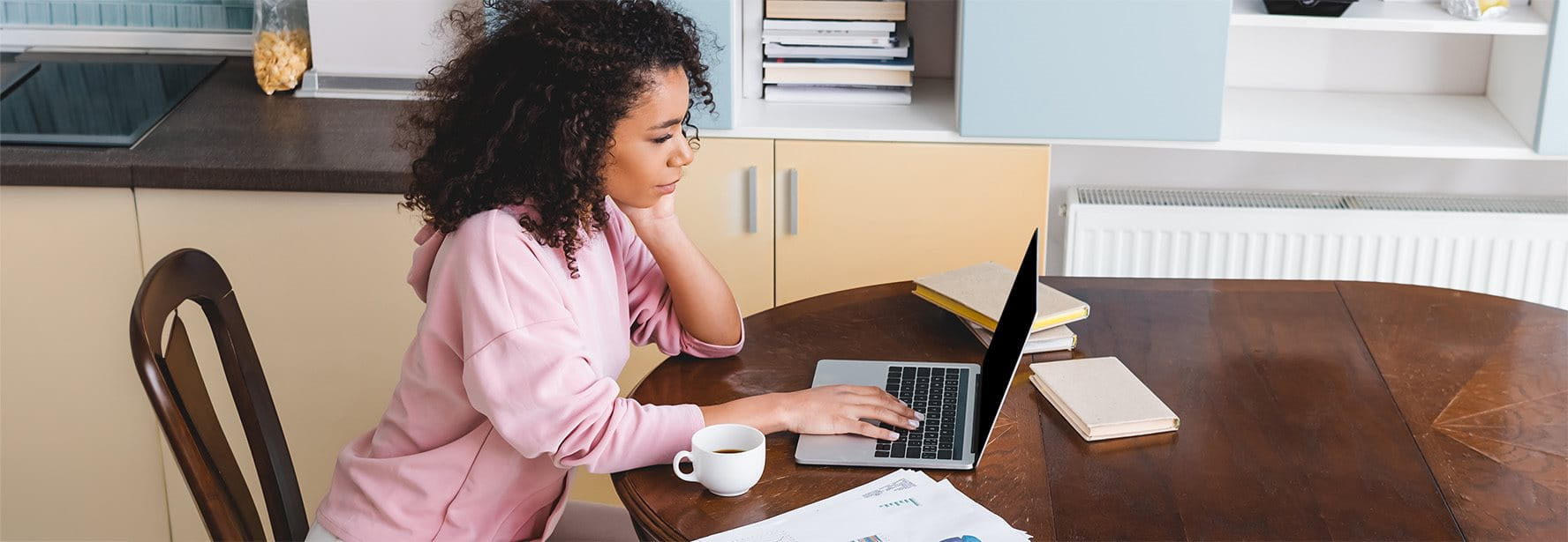 Une femme assise à la table de la cuisine travaille sur un ordinateur portable, des documents fiscaux sont posés à côté d’elle.