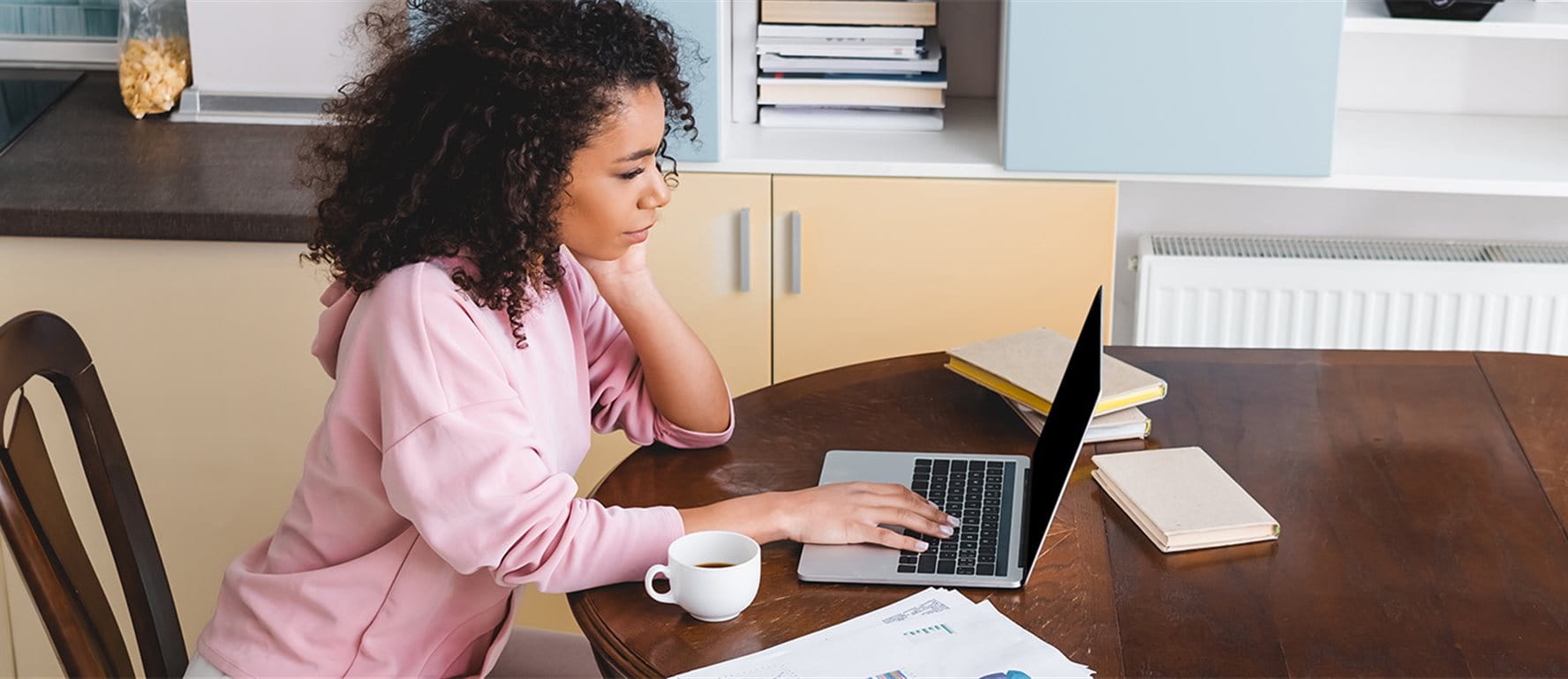 Une femme assise à la table de la cuisine travaille sur un ordinateur portable, des documents fiscaux sont posés à côté d’elle. Une femme assise à la table de la cuisine travaille sur un ordinateur portable, des documents fiscaux sont posés à côté d’elle.