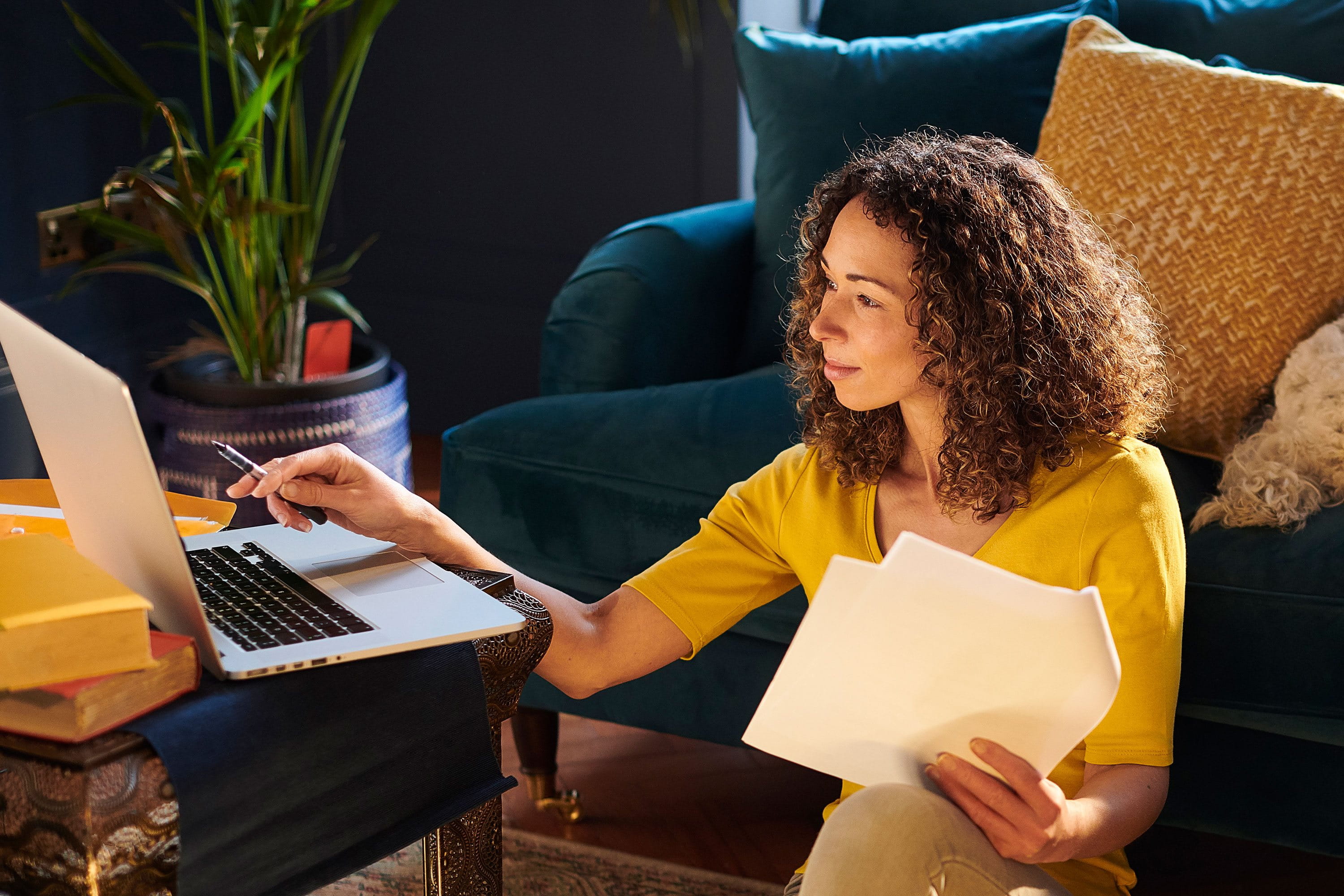 Une femme est assise dans le salon avec son ordinateur portable et examine des documents pour économiser des impôts