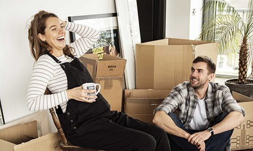 Un couple est assis entre des cartons de déménagement et rit.