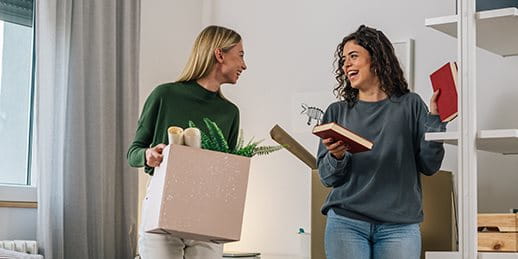 Zwei Frauen lachen und halten Bücher, eine trägt eine Kiste mit Pflanzen. Zwei Frauen lachen und halten Bücher, eine trägt eine Kiste mit Pflanzen.