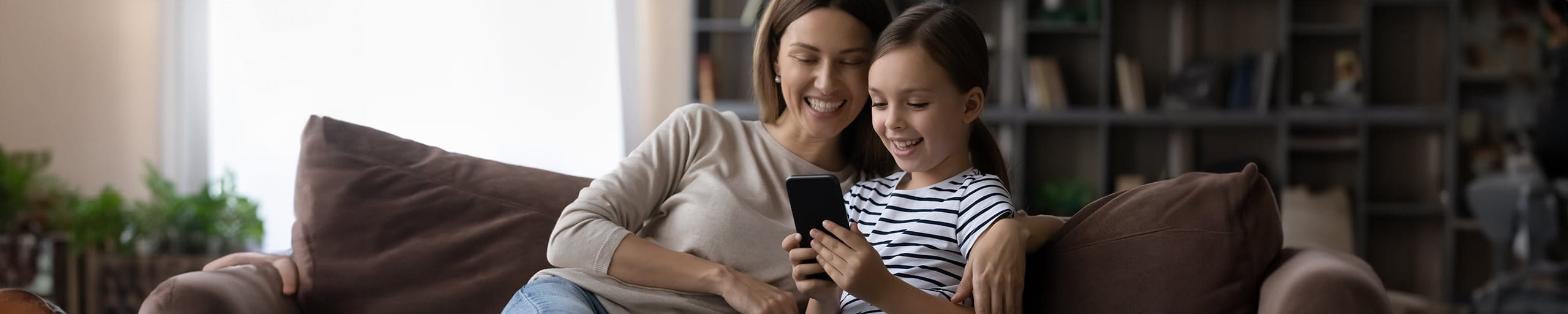 La mère est assise avec sa fille sur le canapé et regarde un smartphone.