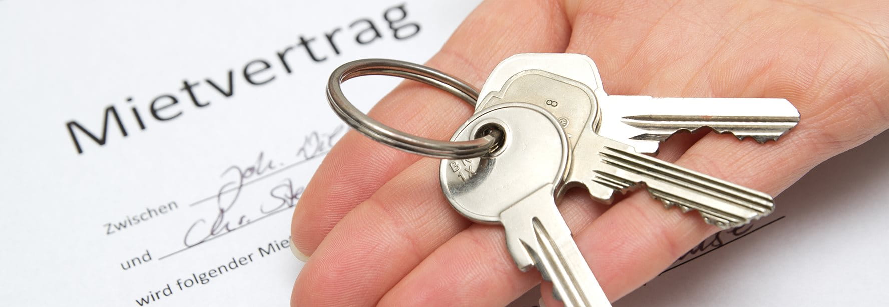 Ein Schlüsselbund liegt in einer offenen Hand über einem Mietvertrag