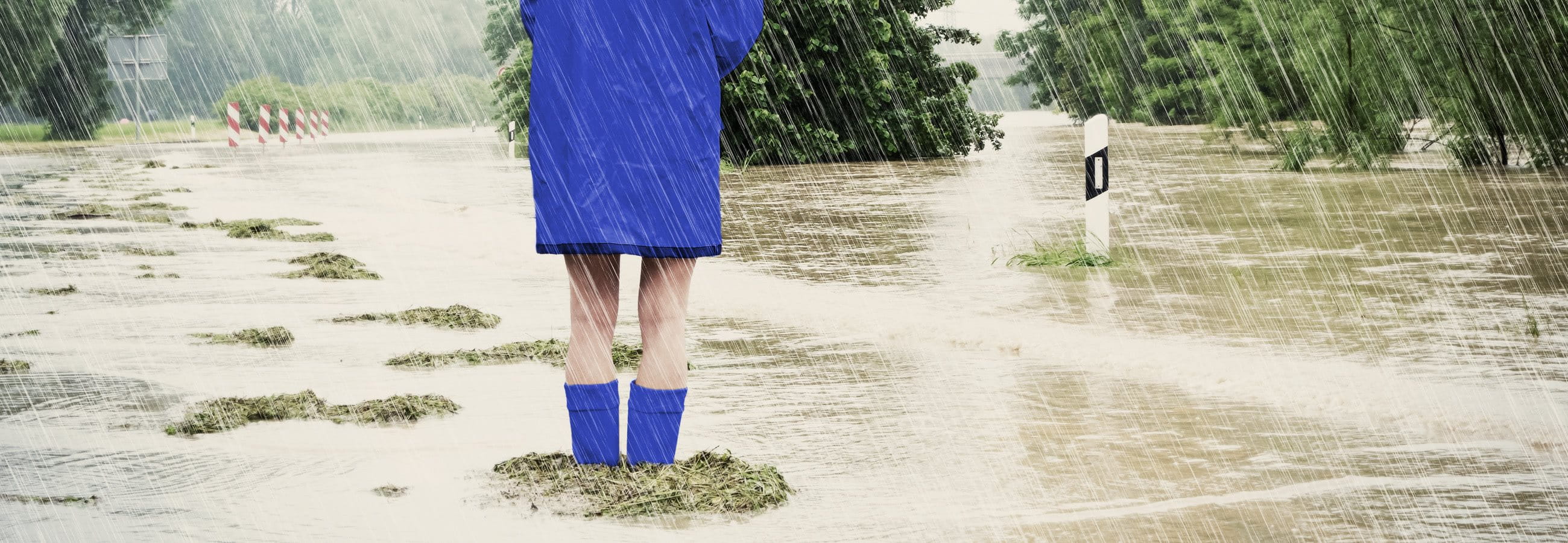 Frau steht mit Regenjacke und Gummistiefel im Hochwasser