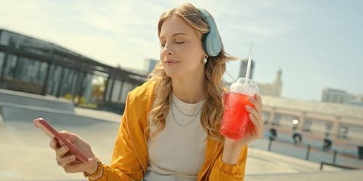 Junges Mädchen hört über Kopfhörer Musik und hält einen Icetea
