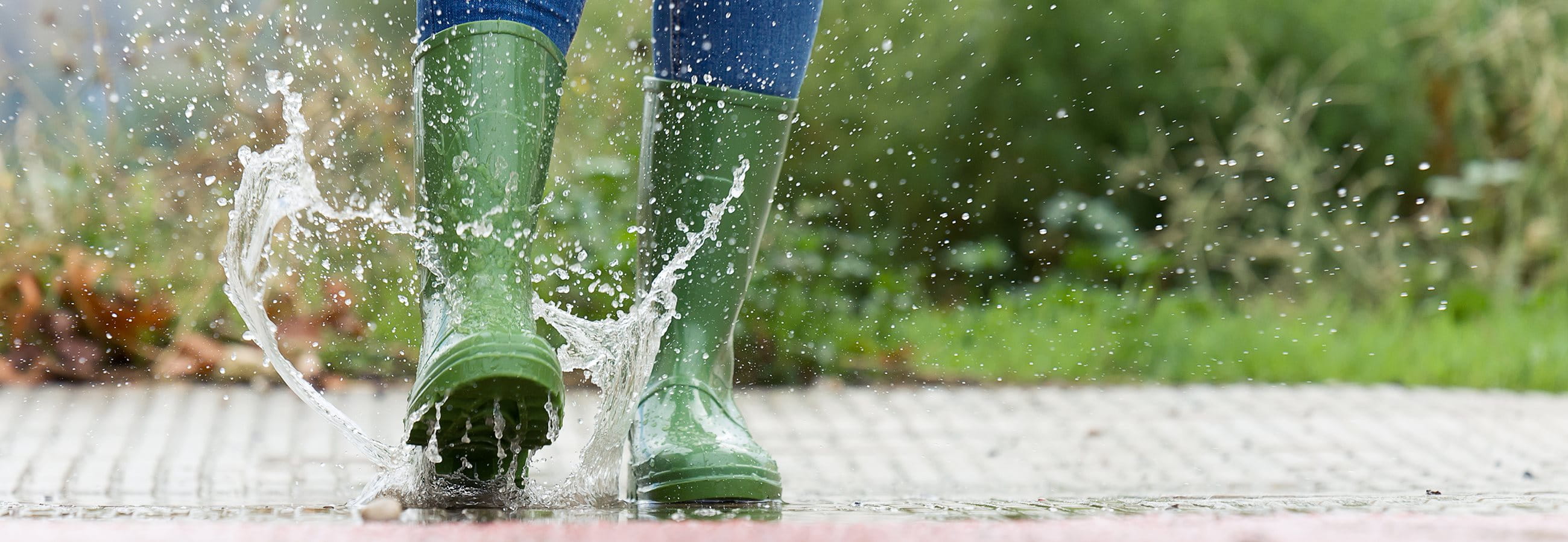 Frau springt in grünen Gummistiefel in eine Pfütze