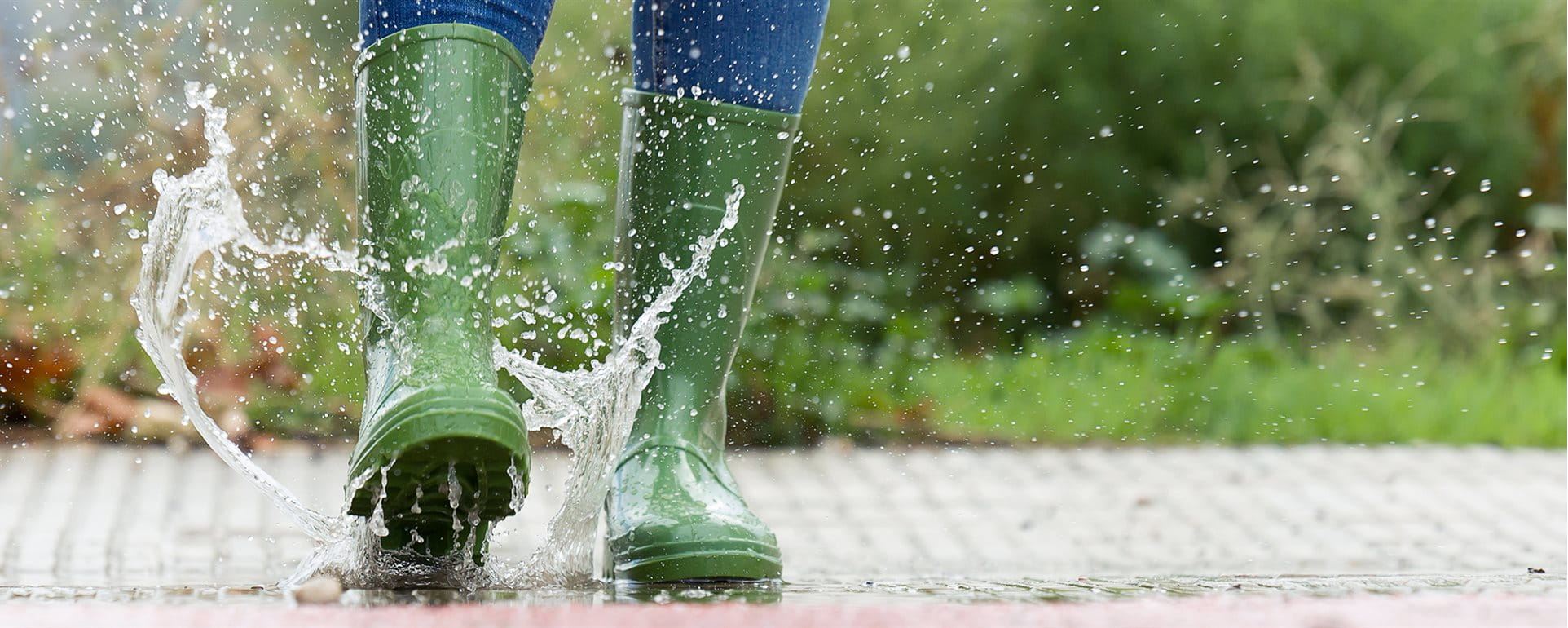 Une femme saute dans une flaque d'eau avec des bottes en vert Une femme saute dans une flaque d'eau avec des bottes en vert