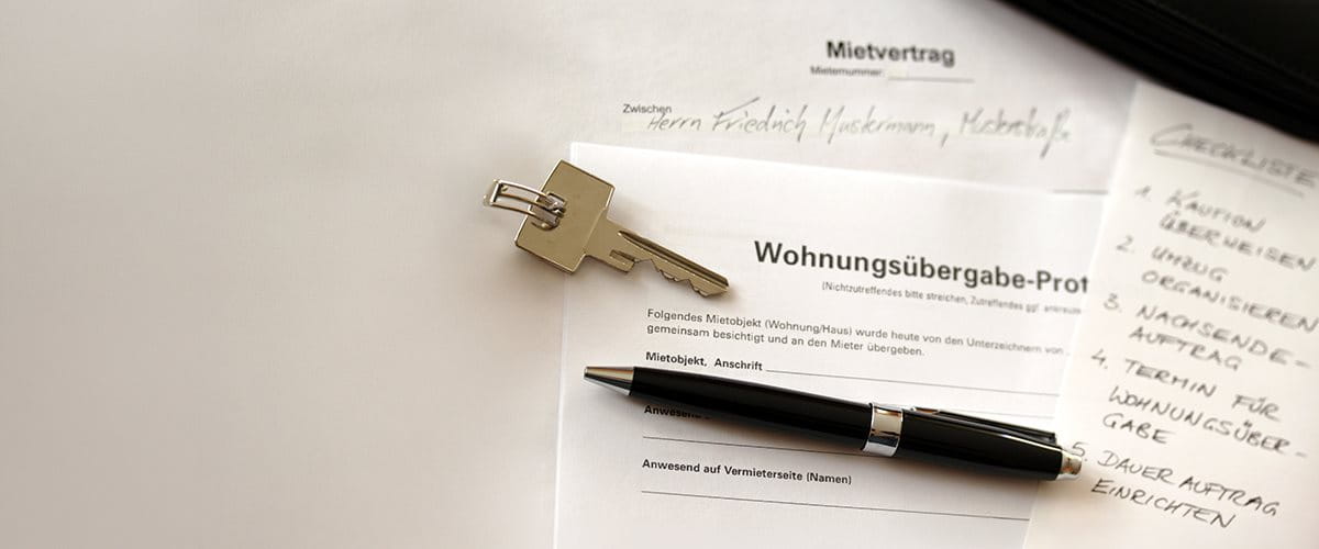 Schlüssel, Stift und Dokumente zu einem Mietvertrag auf einem Tisch.