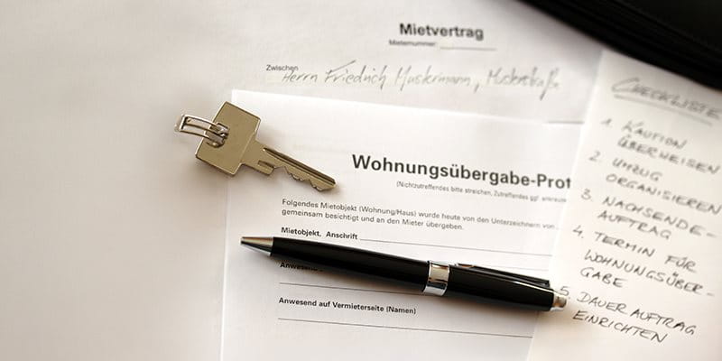 Ein Schlüssel liegt neben einem Mietvertrag und einem Protokoll zur Wohnungsübergabe.