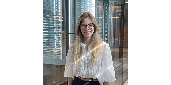 Eine Frau mit langen blonden Haaren und Brille lächelt in einem modernen Raum.