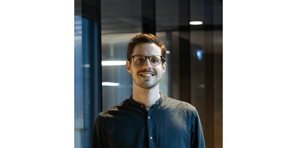 Ein Mann mit Brille lächelt in einem modernen Raum mit Glaswänden.