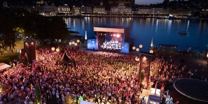 Open-Air-Konzert mit Musikerinnen und Musikern vor See- und Stadtkulisse.