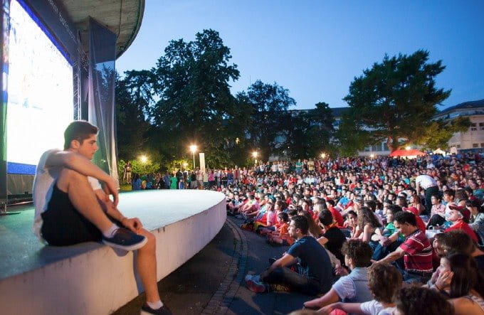 Une grande foule est assise au sol pendant un événement sur une scène extérieure.