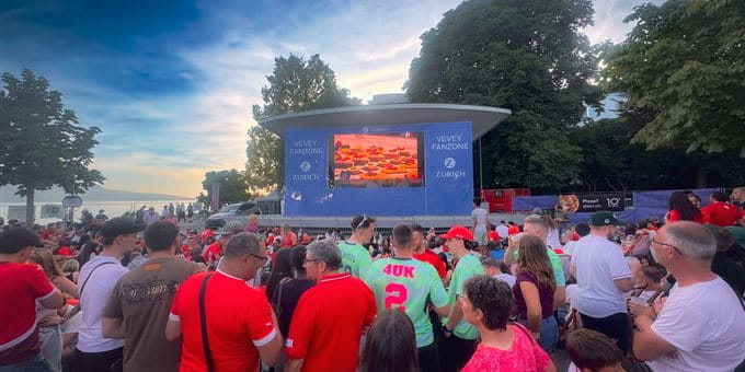Una grande folla di persone è seduta a terra mentre si svolge un evento su un palco all'aperto. Una grande folla di persone è seduta a terra mentre si svolge un evento su un palco all'aperto.