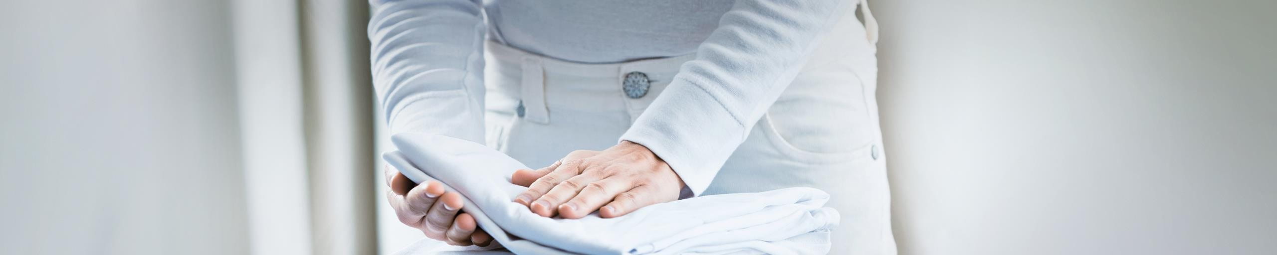 Una persona piega dei tessuti di lino sul tavolo da stiro.