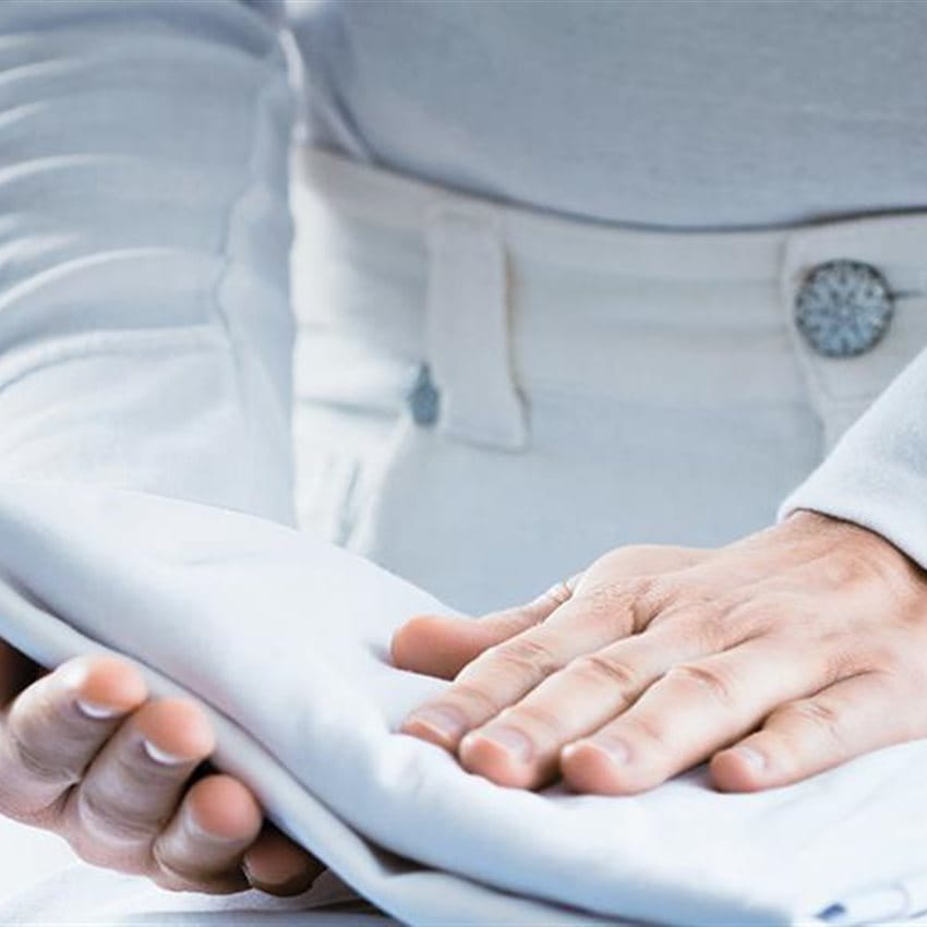 Eine Person faltet Leinentücher auf einem Bügelbrett. Eine Person faltet Leinentücher auf einem Bügelbrett.