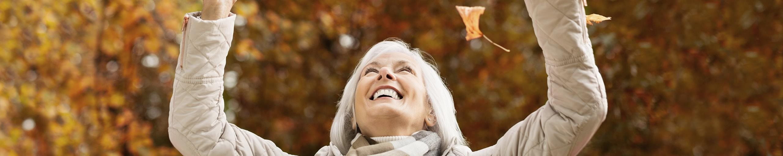 Eine ältere Frau spielt mit Laub.