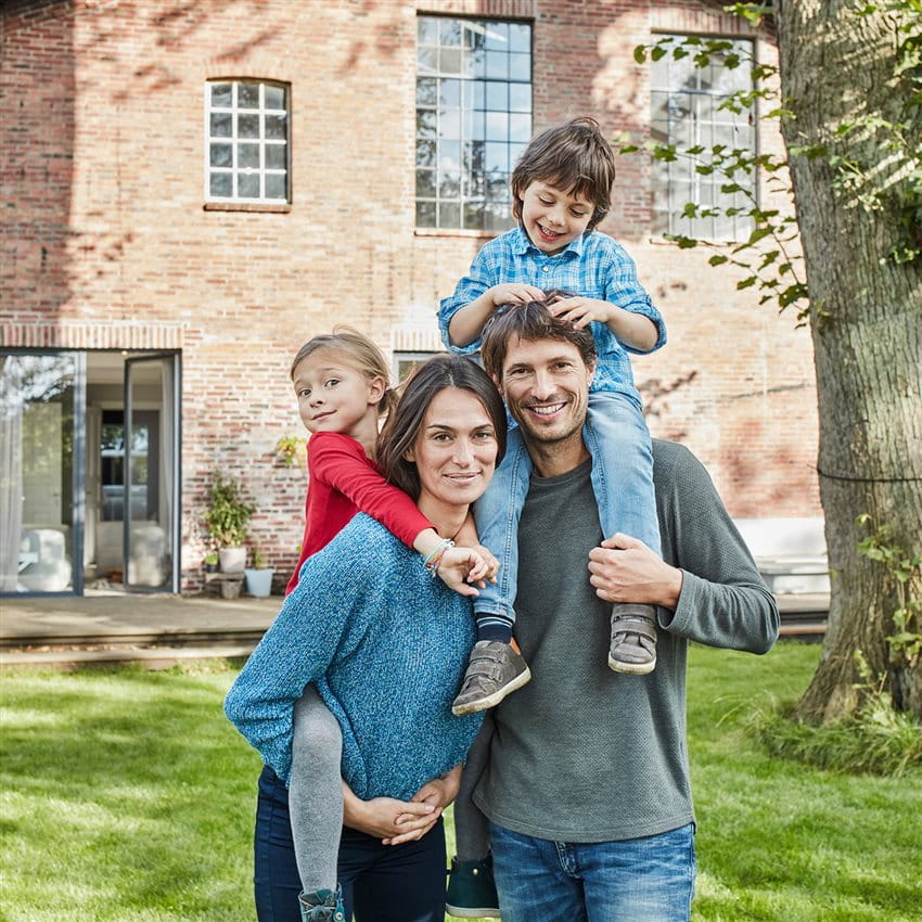 Una famiglia è riunita in giardino davanti a una casa di mattoni. Un bambino è seduto sulle spalle del padre, un altro viene tenuto in braccio dalla madre. Una famiglia è riunita in giardino davanti a una casa di mattoni. Un bambino è seduto sulle spalle del padre, un altro viene tenuto in braccio dalla madre.